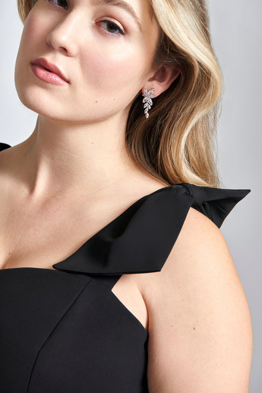 Front detailed view of a woman wearing a black stretch viscose fuller bust dropped waist dress with full skirt and shoulder bows designed by Miriam Baker.