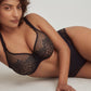 A woman lying down wearing the DD+ Madison Unpadded Seamless T-Shirt Bra in Black with matching cheeky by PrimaDonna.