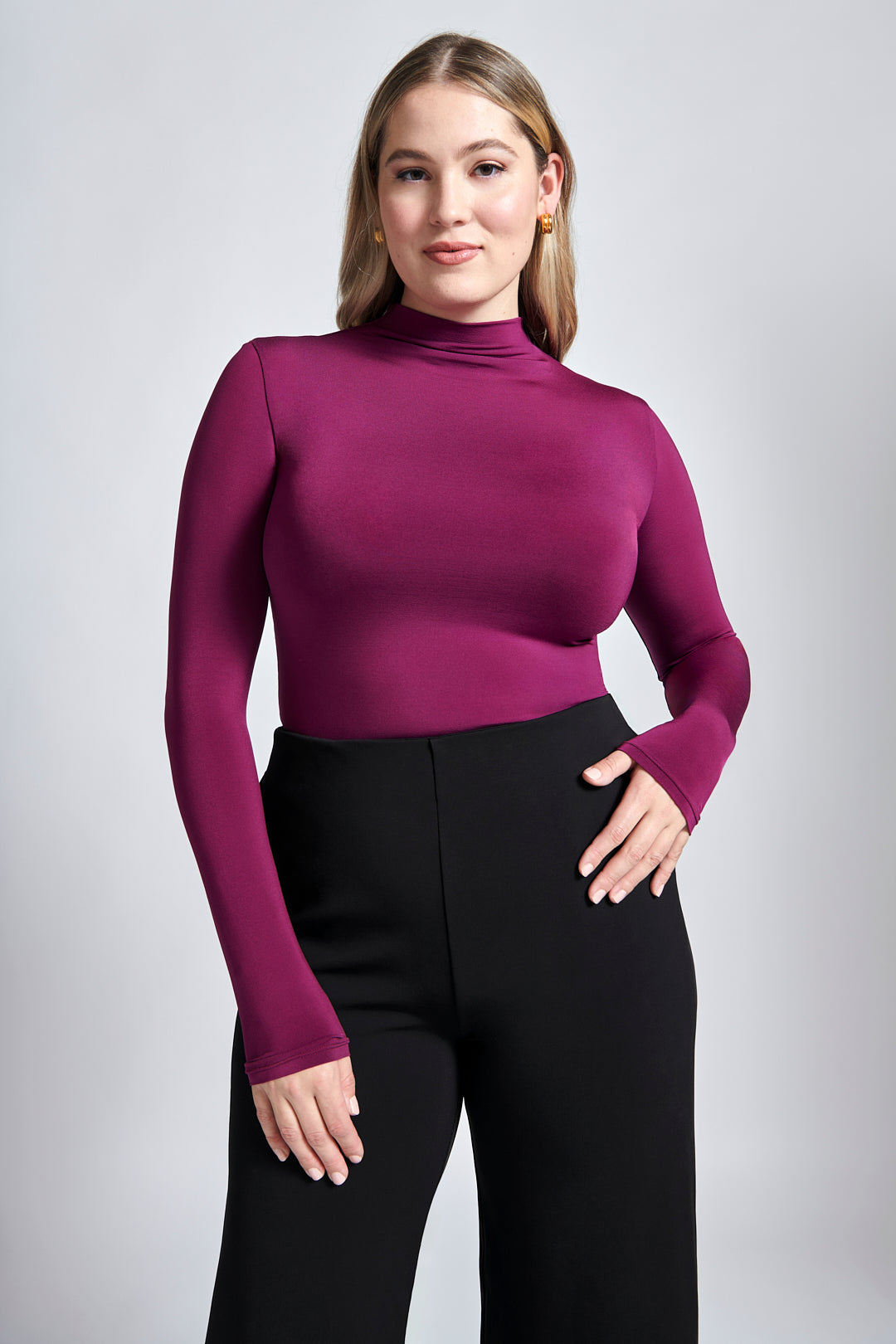 Front view of a size 12 woman wearing a fuller bust mock neck pullover in violet paired with black high waisted wide leg trousers featuring in-seam pockets.