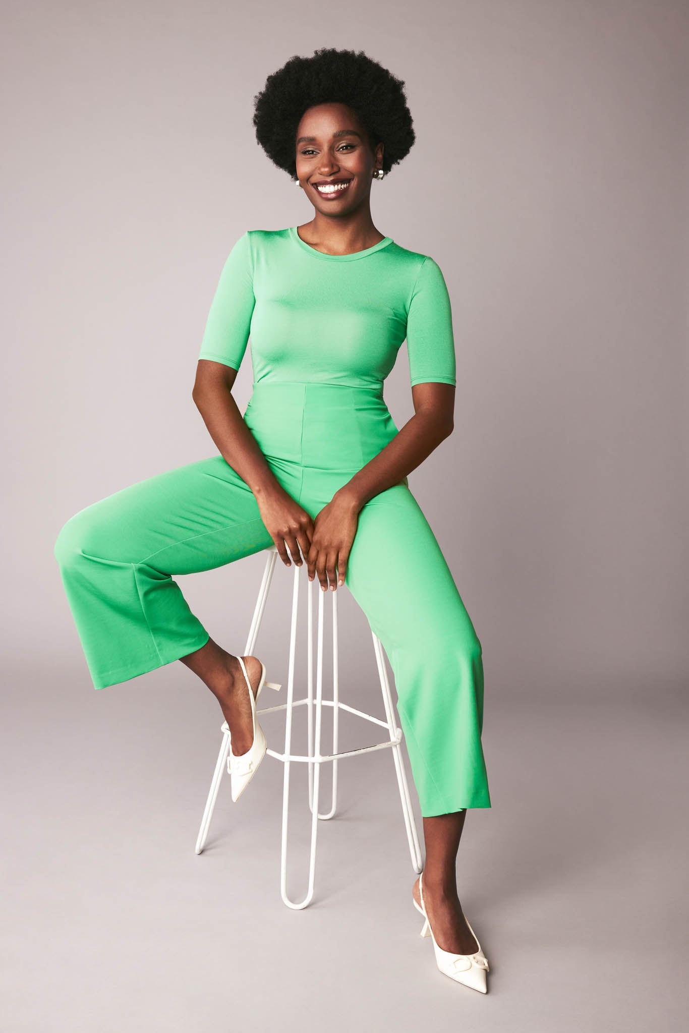 Front view of a woman sitting, wearing a half sleeve crew neck fuller bust T-shirt paired with matching wide leg cropped pants in vibrant kiwi green by Miriam Baker.