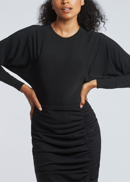 Front view of woman wearing a dolman sleeve batwing pullover in black bamboo paired with a stretch crepe ruched pencil skirt by Miriam Baker.