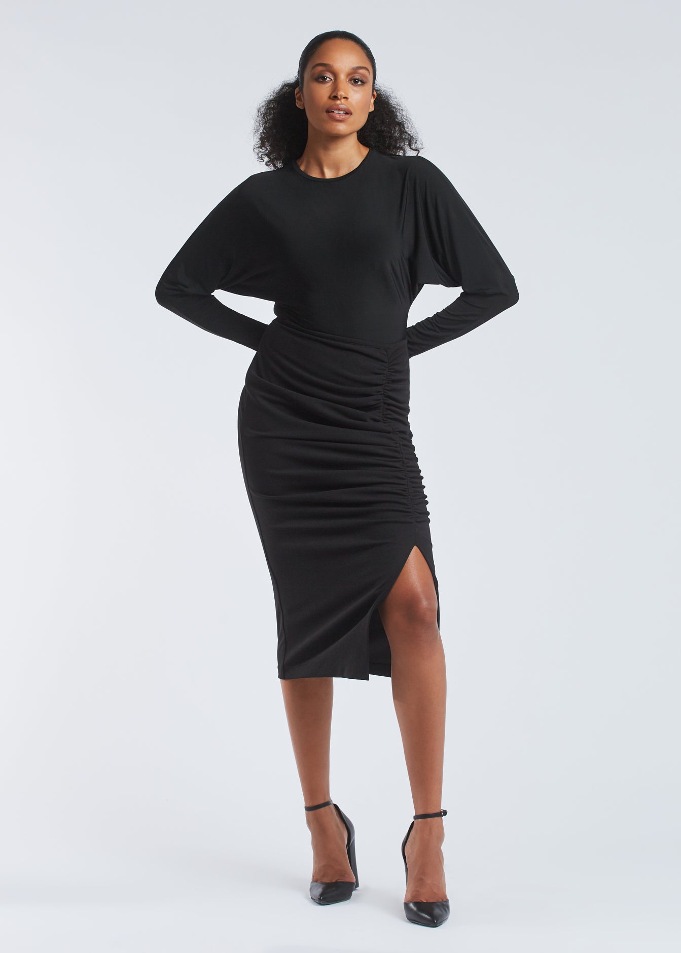 Front view of woman wearing a dolman sleeve batwing pullover in black bamboo paired with a stretch crepe ruched pencil skirt by Miriam Baker.