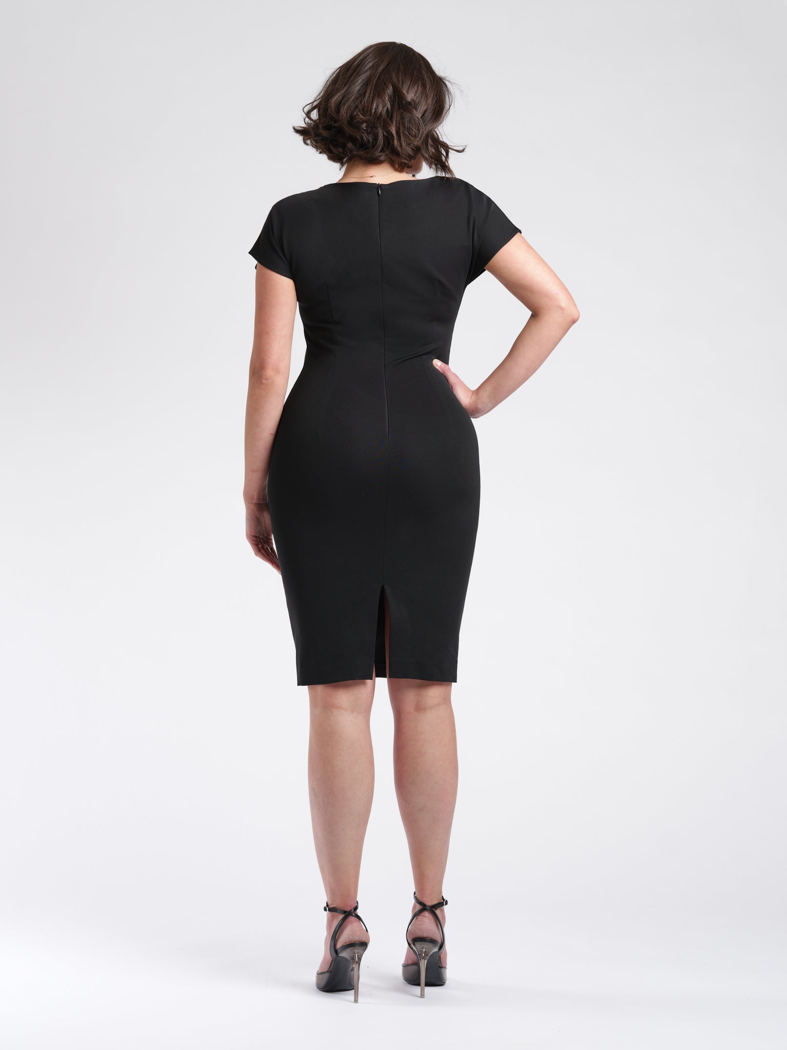 Back view of a woman wearing a black fuller bust stretch viscose dress with side draping details and short kimono sleeves designed by Miriam Baker.