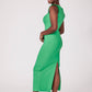 Side view of a woman wearing a green stretch viscose fuller bust midi length bodycon dress with shoulder ruffles and a back slit designed by Miriam Baker.