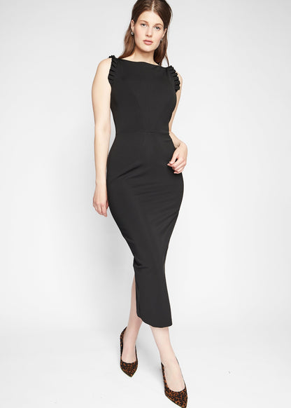 Front view of a woman wearing a black stretch viscose fuller bust midi length bodycon dress with shoulder ruffles and a back slit designed by Miriam Baker.