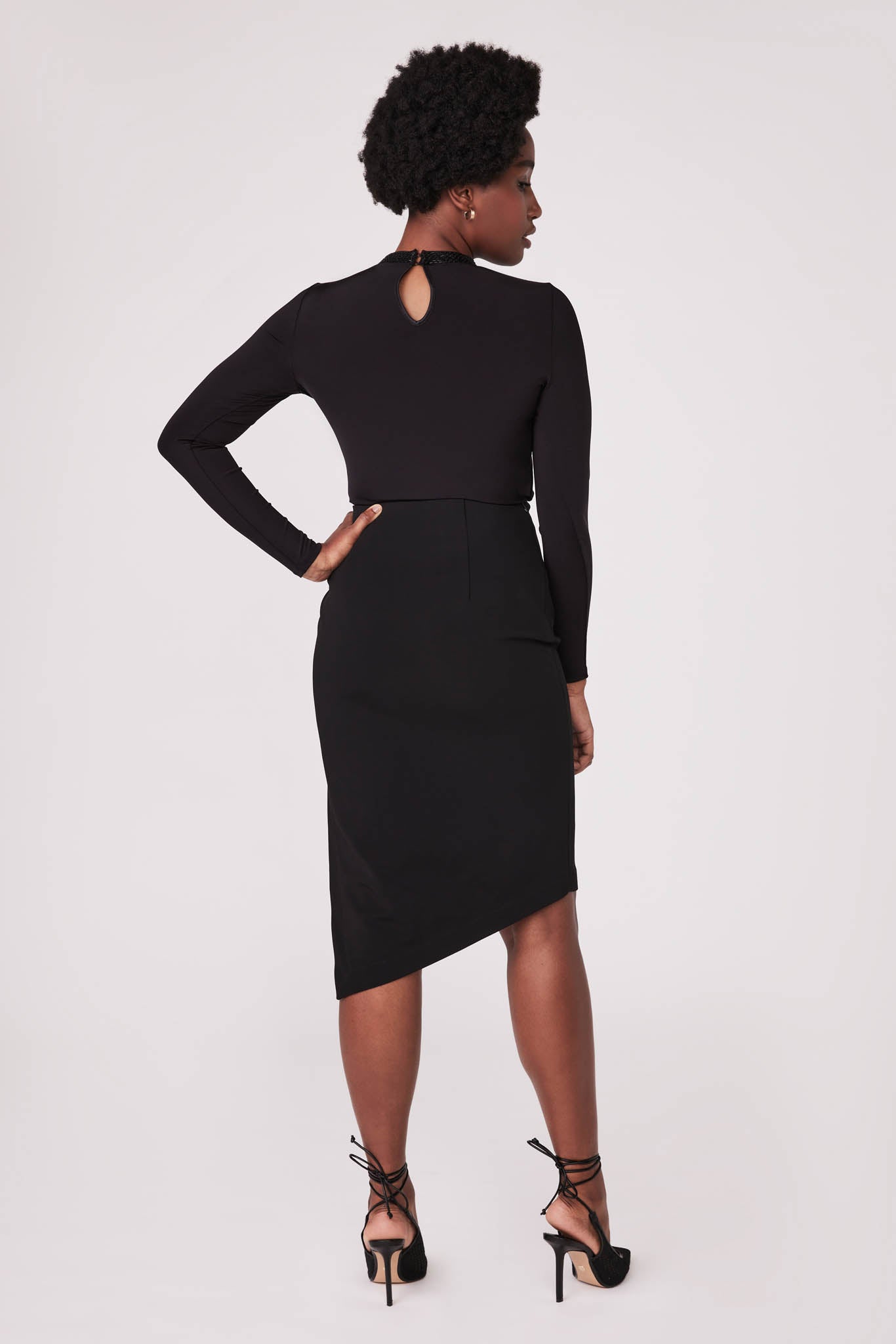 Back view of a woman wearing a high waisted black asymmetrical pencil skirt with cut out detail by Miriam Baker.