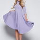 Front view of a woman wearing a asymmetric mock neck fuller bust dress with 3/4 length sleeves and side seam pockets in lilac stretch viscose fabric by Miriam Baker.