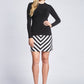 Front view of a woman wearing a black pullover paired with a black and white chevron stripe A-line mini skirt with side seam pockets designed by Miriam Baker.