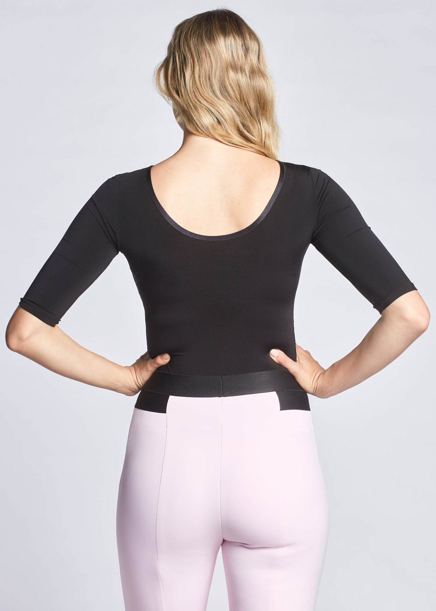 Back view of a woman wearing a black fuller bust stretch viscose half sleeve boatneck pullover with back scoop neck designed by Miriam Baker.