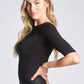 Side view of a woman wearing a black fuller bust stretch viscose half sleeve boatneck pullover with back ballerina scoop neck designed by Miriam Baker.