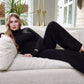 Woman lounging on a sofa wearing a black stretch viscose fuller bust long sleeve mock neck pullover by Miriam Baker.