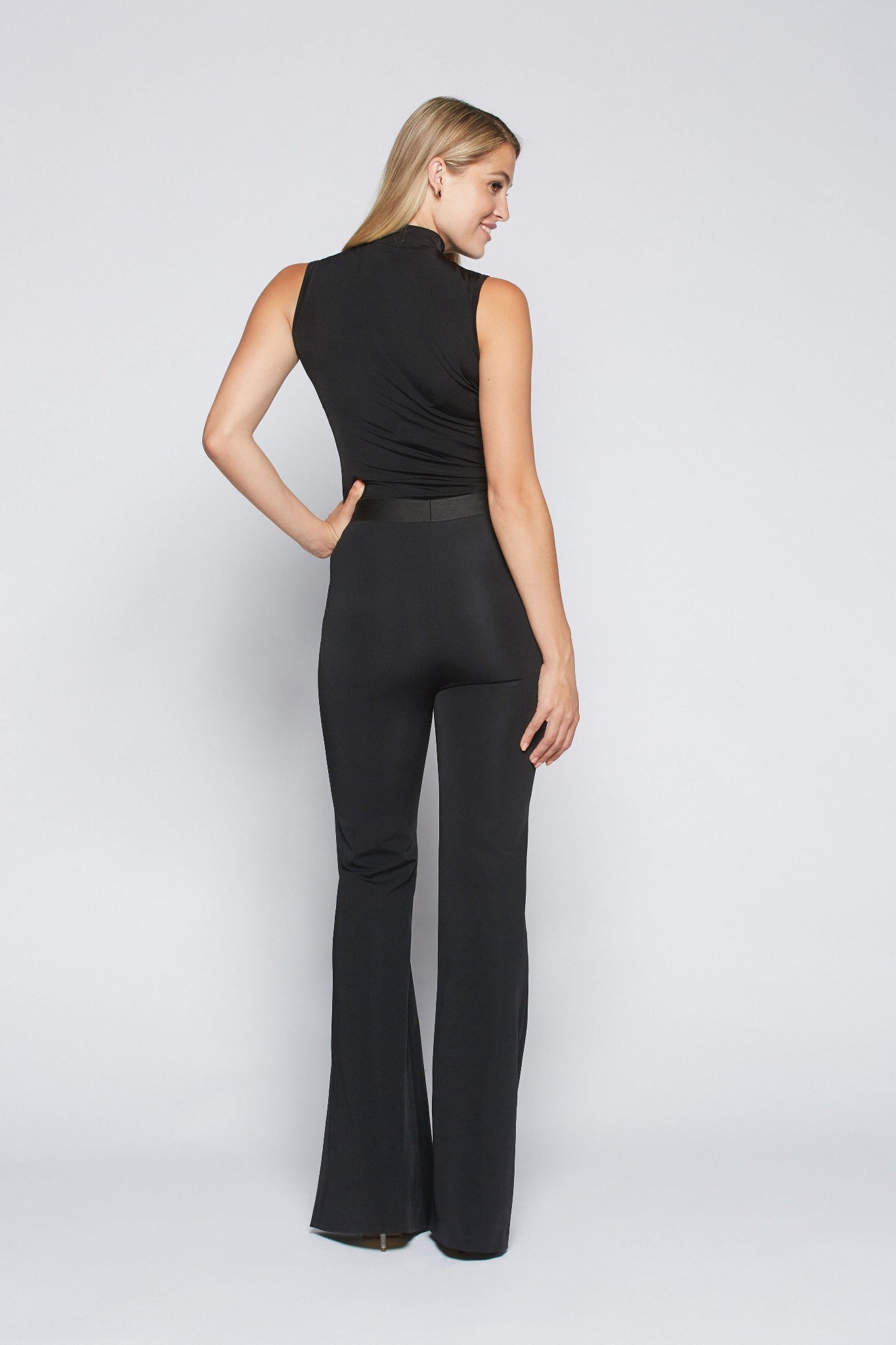 Back view of a woman wearing a pair of hight waisted stretch viscose bell bottom trousers with an elastic waist and functional slash pockets with exposed zippers by Miriam Baker.