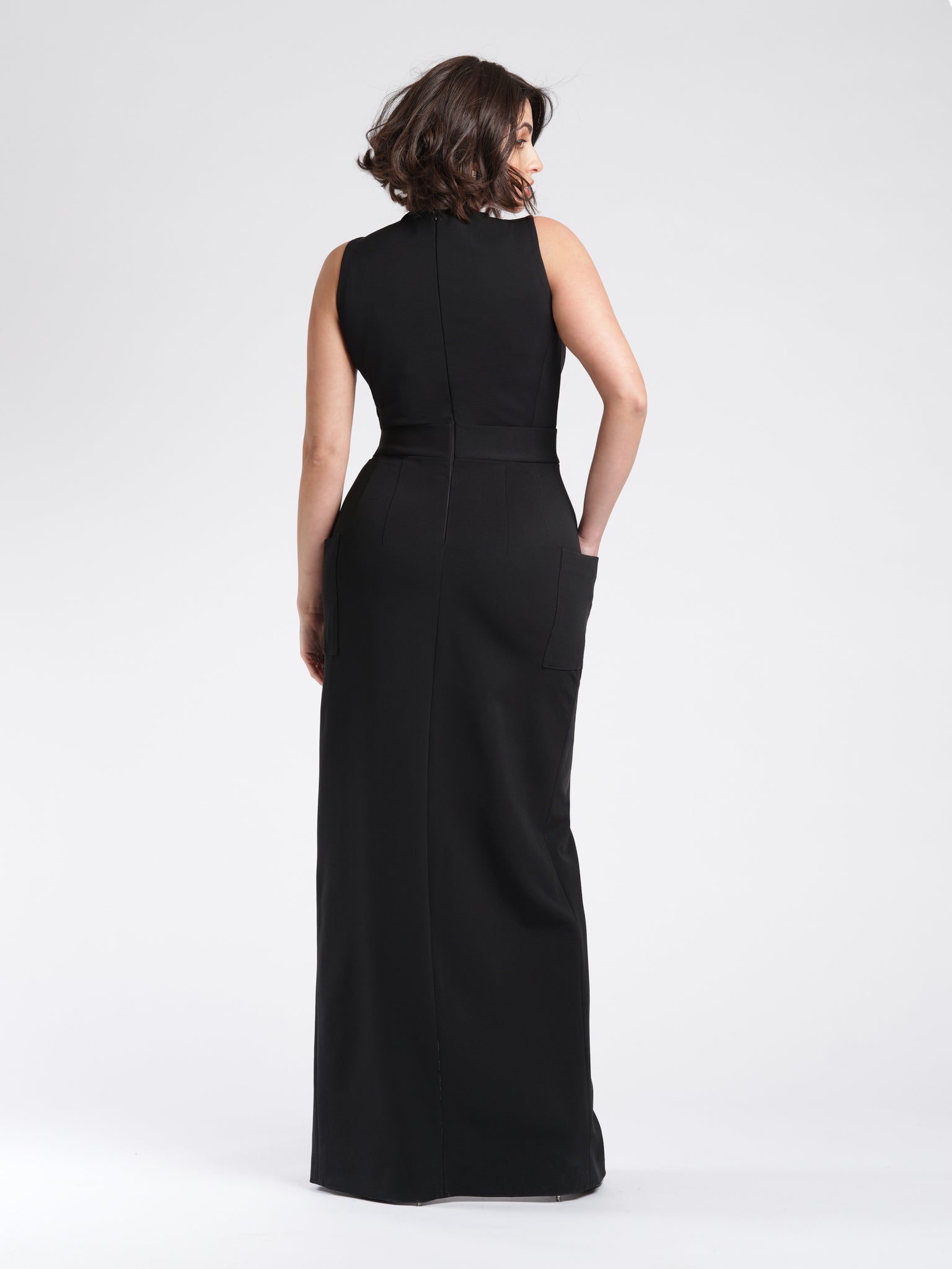 Back view of a size 6 woman wearing a luxury fuller bust stretch viscose evening dress with oversized patch pockets and waist sash detail by Miriam Baker.