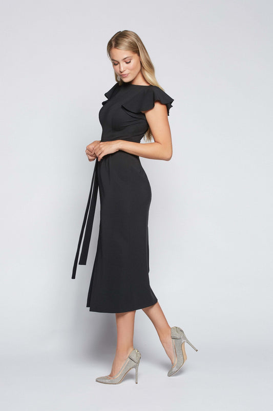 Side view of a woman wearing a black stretch viscose fuller bust boatneck midi dress with front slit, waist sash, and flutter sleeves designed by Miriam Baker.