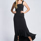 Front view of a woman wearing a black stretch viscose fuller bust empire waist gown with high low flounce hem and shoulder bow detail designed by Miriam Baker.