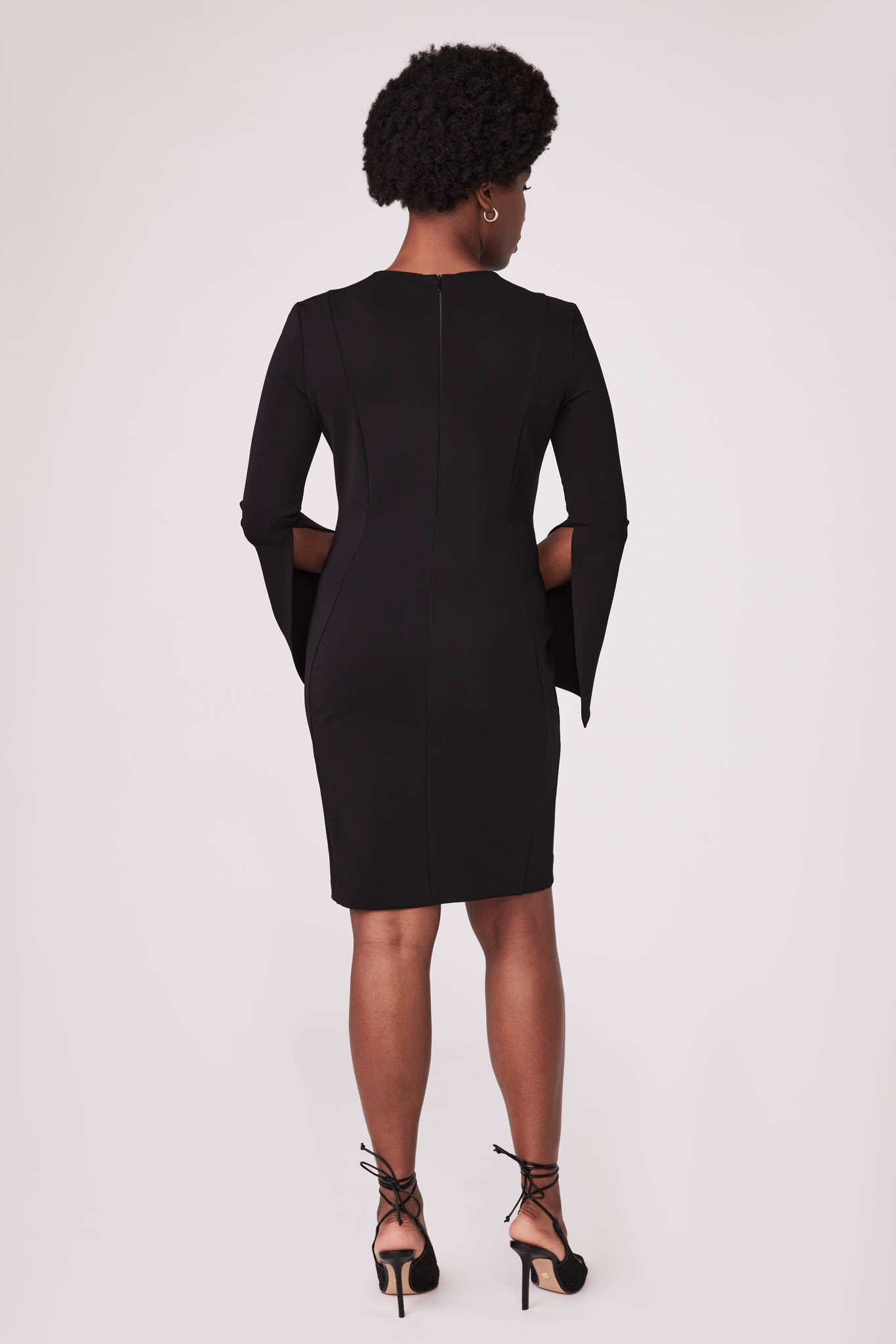 Back view of a woman wearing a black stretch viscose fuller bust princess line split sleeve bodycon dress with a crew neck and invisible zipper designed by Miriam Baker.