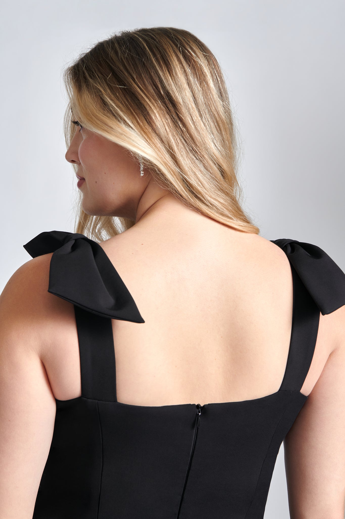 Back close up detailed view of a woman wearing a black stretch viscose fuller bust dropped waist dress with full skirt and shoulder bows designed by Miriam Baker.