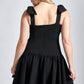 Back view of a woman wearing a black stretch viscose fuller bust dropped waist dress with full skirt and shoulder bows designed by Miriam Baker.