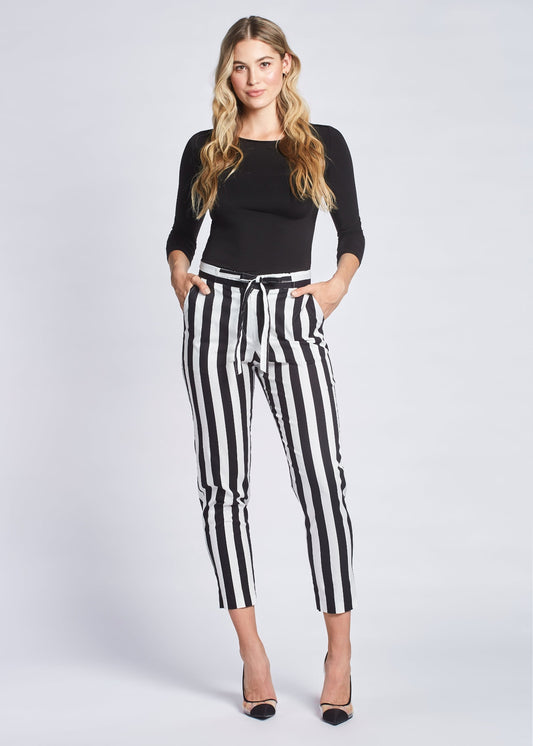 Front view of a woman wearing a pair of black and white stripe crop pants with slash pockets, a fly front, and drawstring waist designed by Miriam Baker.