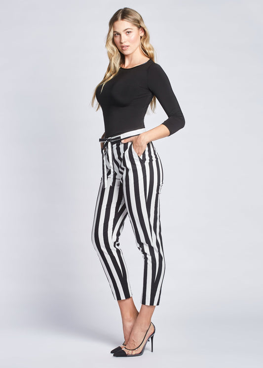 Side view of a woman wearing a pair of black and white stripe crop pants with slash pockets, a fly front, and drawstring waist designed by Miriam Baker.