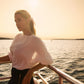 Woman on a boat at sunset wearing a cream coloured lurex linen boatneck fuller bust blouse with wrist ruffles and an elastic waist designed by Miriam Baker.