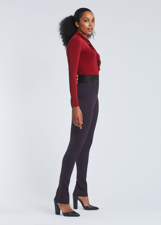 Side view of a woman wearing high waisted full length stretch trousers in navy blue with an exposed zipper at the hem designed by Miriam Baker.