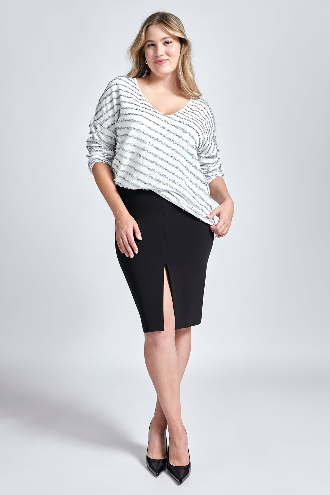 Front view of a woman wearing a recycled cotton v-neck sweater paired with a black stretch viscose skirt with a front slit by Miriam Baker.