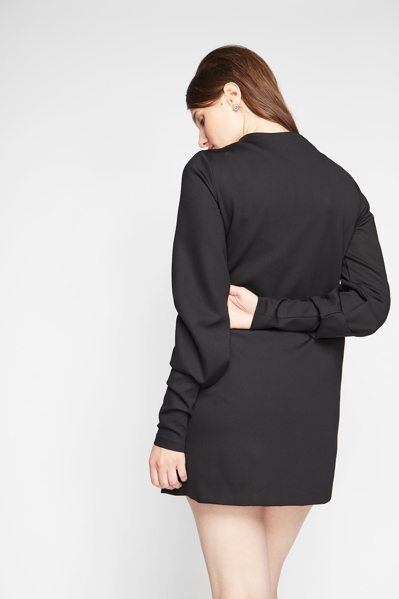 Back view of a woman wearing a long sleeve fuller bust mock neck shift dress with pockets in black stretch jersey designed by Miriam Baker.