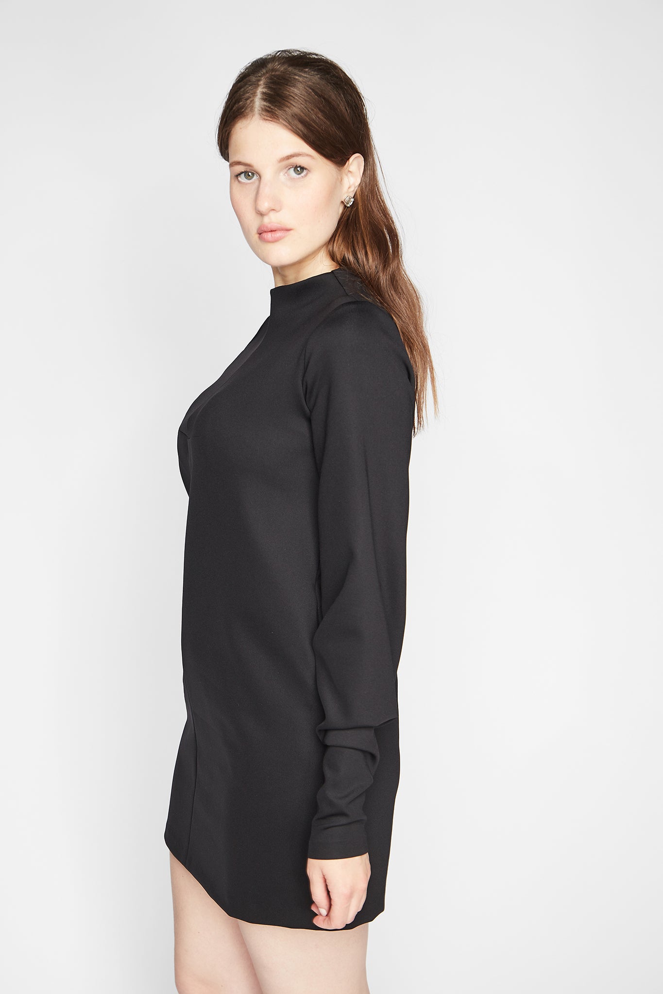Side view of a woman wearing a long sleeve fuller bust mock neck shift dress with pockets in black stretch jersey designed by Miriam Baker.