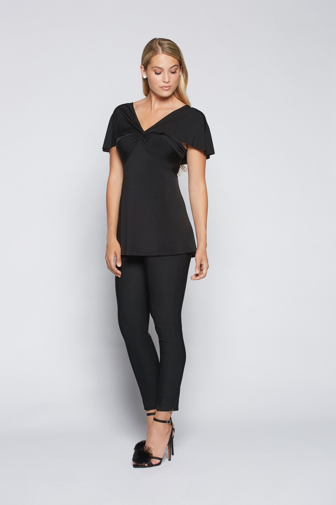 Woman wearing a fuller bust low cut v-neck top with a butterfly twist detail at the empire waist in black stretch viscose jersey by Miriam Baker.