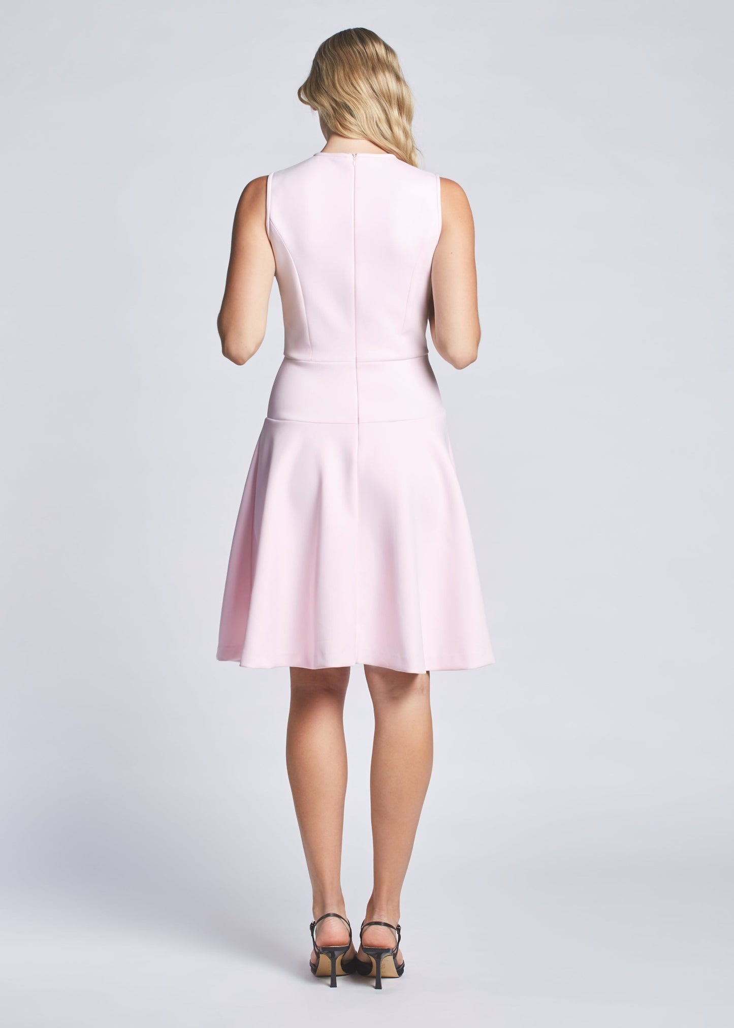 Back view of a woman wearing a baby pink fit and flare fuller bust sleeveless crew neck dress with invisible zipper by Miriam Baker.