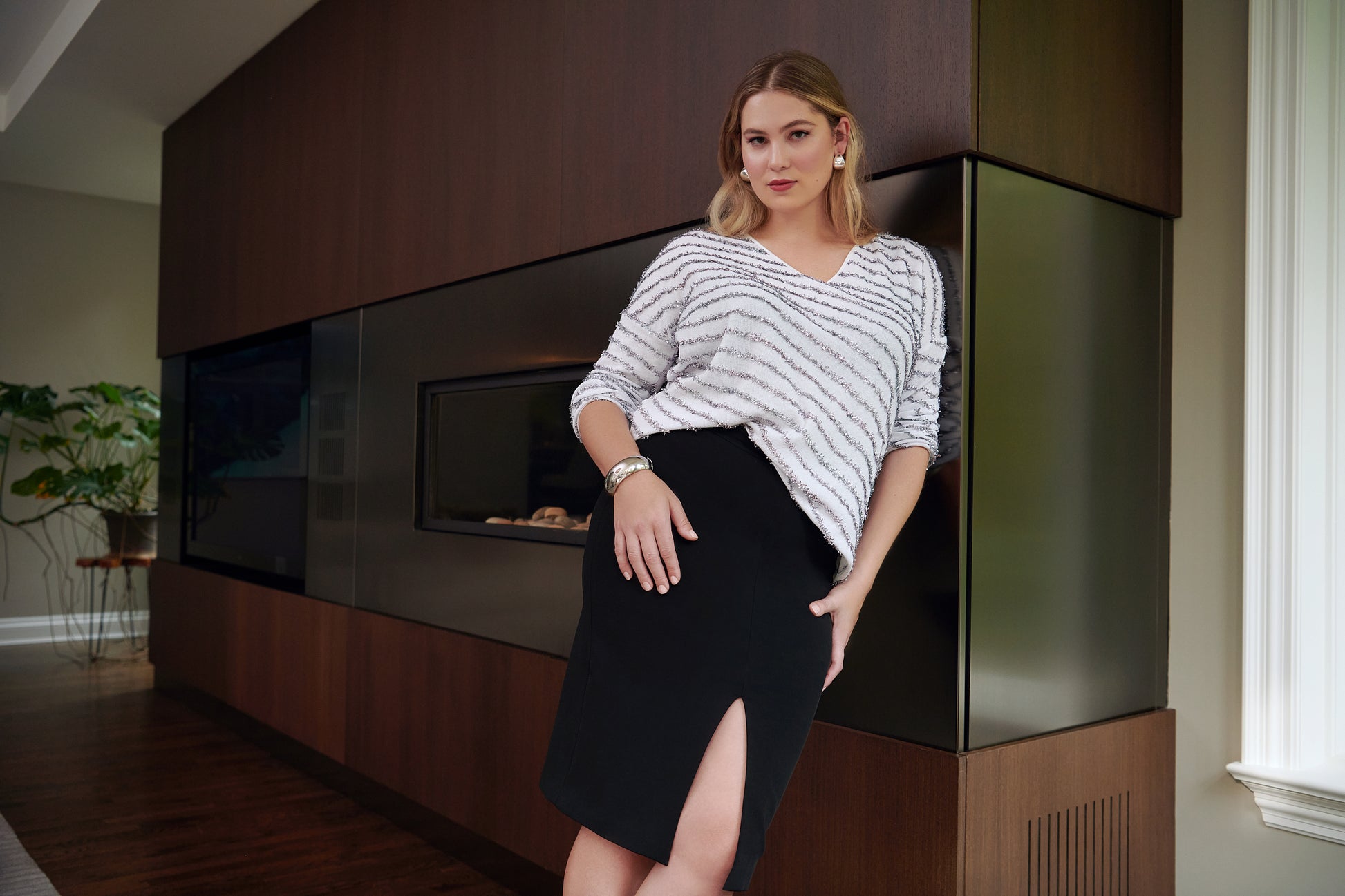Front view of a woman wearing a recycled cotton v-neck sweater paired with a black stretch viscose skirt with a front slit by Miriam Baker.