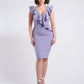 Woman wearing a stretch viscose fuller bust v-neck sheath dress with ruffles that frame the neckline in lilac designed by Miriam Baker.