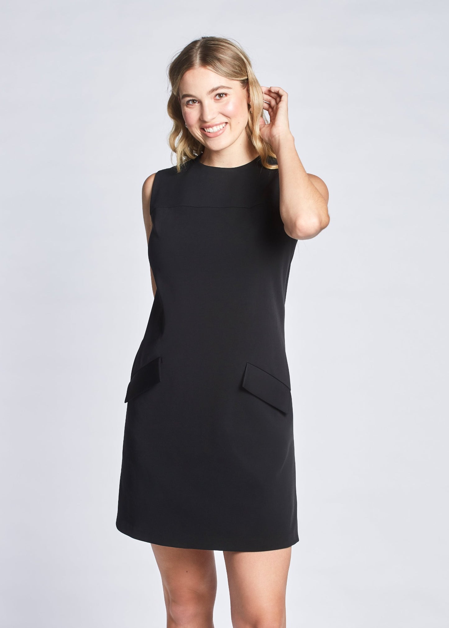 Woman wearing a black semi-fitted-fuller bust A-line shift dress with a crew neck and welt pockets designed by Miriam Baker.