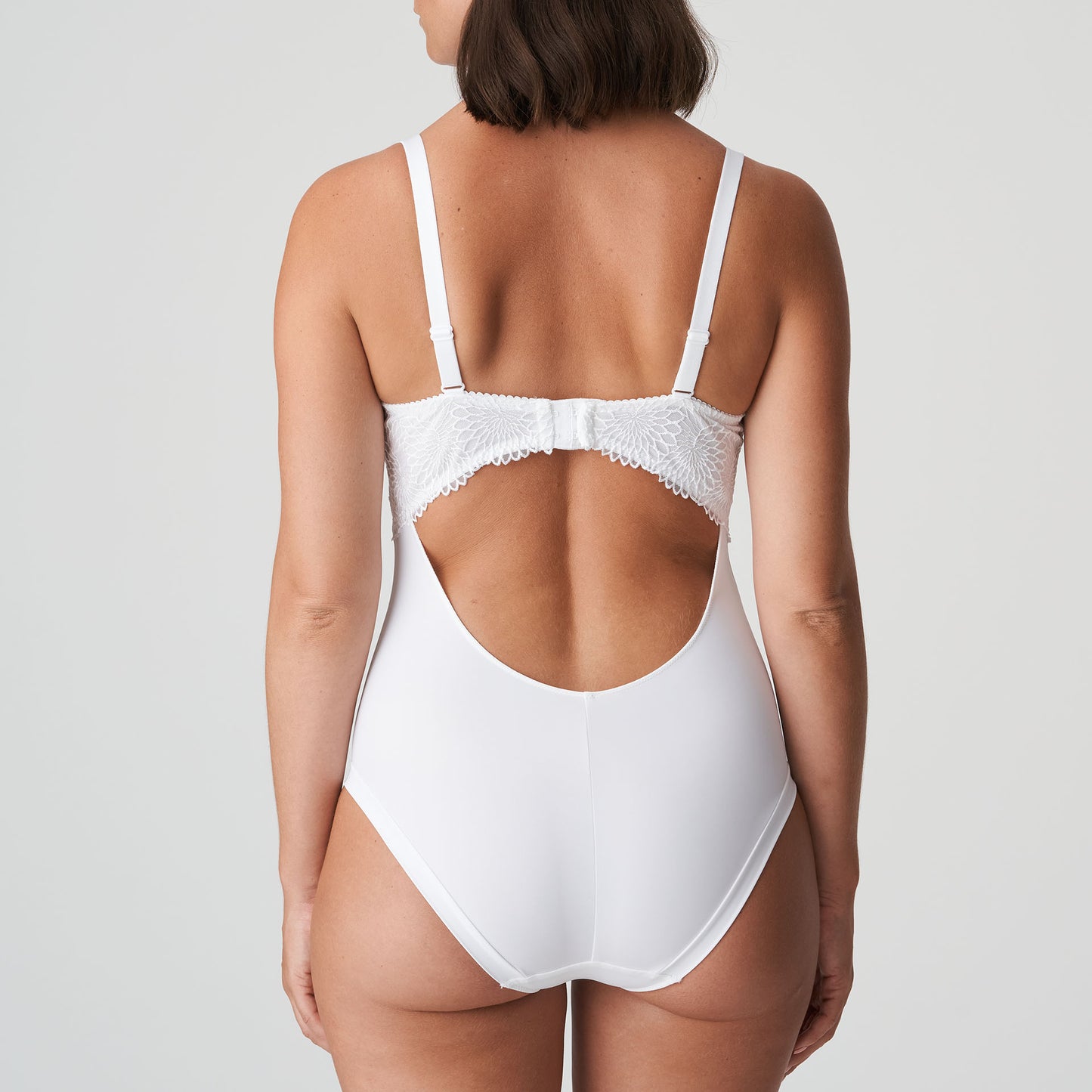 Back view of a woman wearing a DD+ open back bodysuit with built in full support underwire bra in white by Primadonna.