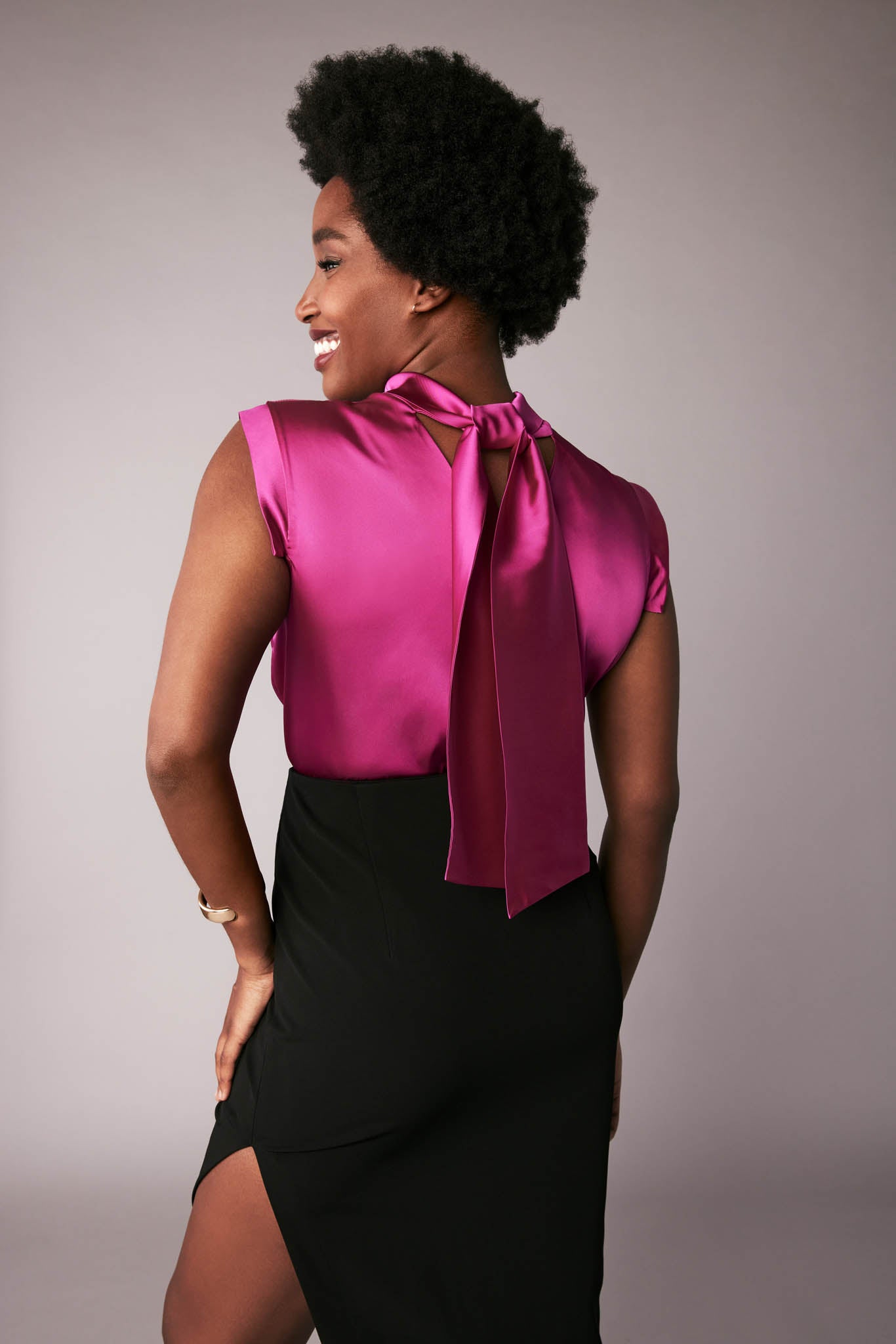 Back view of a woman wearing a fuchsia stretch silk charmeuse fuller bust blouse with bust darts and pussy bow collar designed by Miriam Baker.