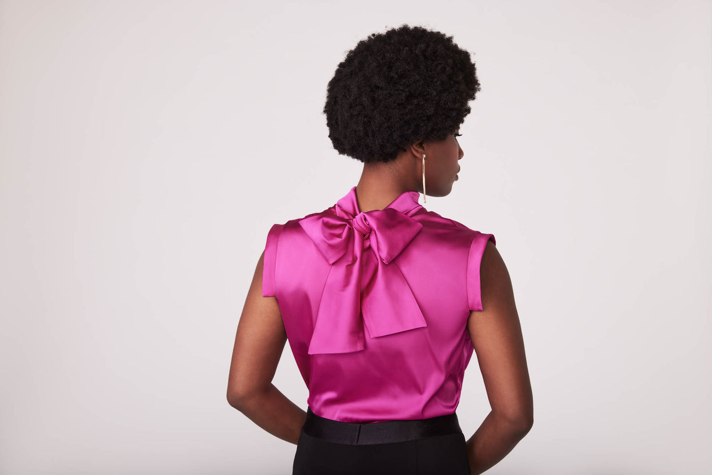 Back view of a woman wearing a fuchsia stretch silk charmeuse fuller bust blouse with bust darts and pussy bow collar designed by Miriam Baker.