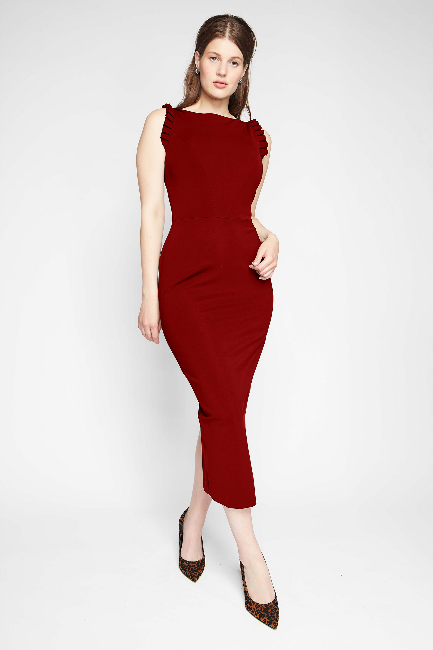 Front view of a woman wearing a red stretch viscose fuller bust midi length bodycon dress with shoulder ruffles and a back slit designed by Miriam Baker.