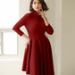 Front view of a woman wearing an asymmetric mock neck fuller bust dress with 3/4 length sleeves and side seam pockets in red stretch viscose fabric by Miriam Baker.