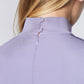 Detailed back view of a woman wearing an asymmetric mock neck fuller bust dress with 3/4 length sleeves and side seam pockets in lilac stretch viscose fabric by Miriam Baker.