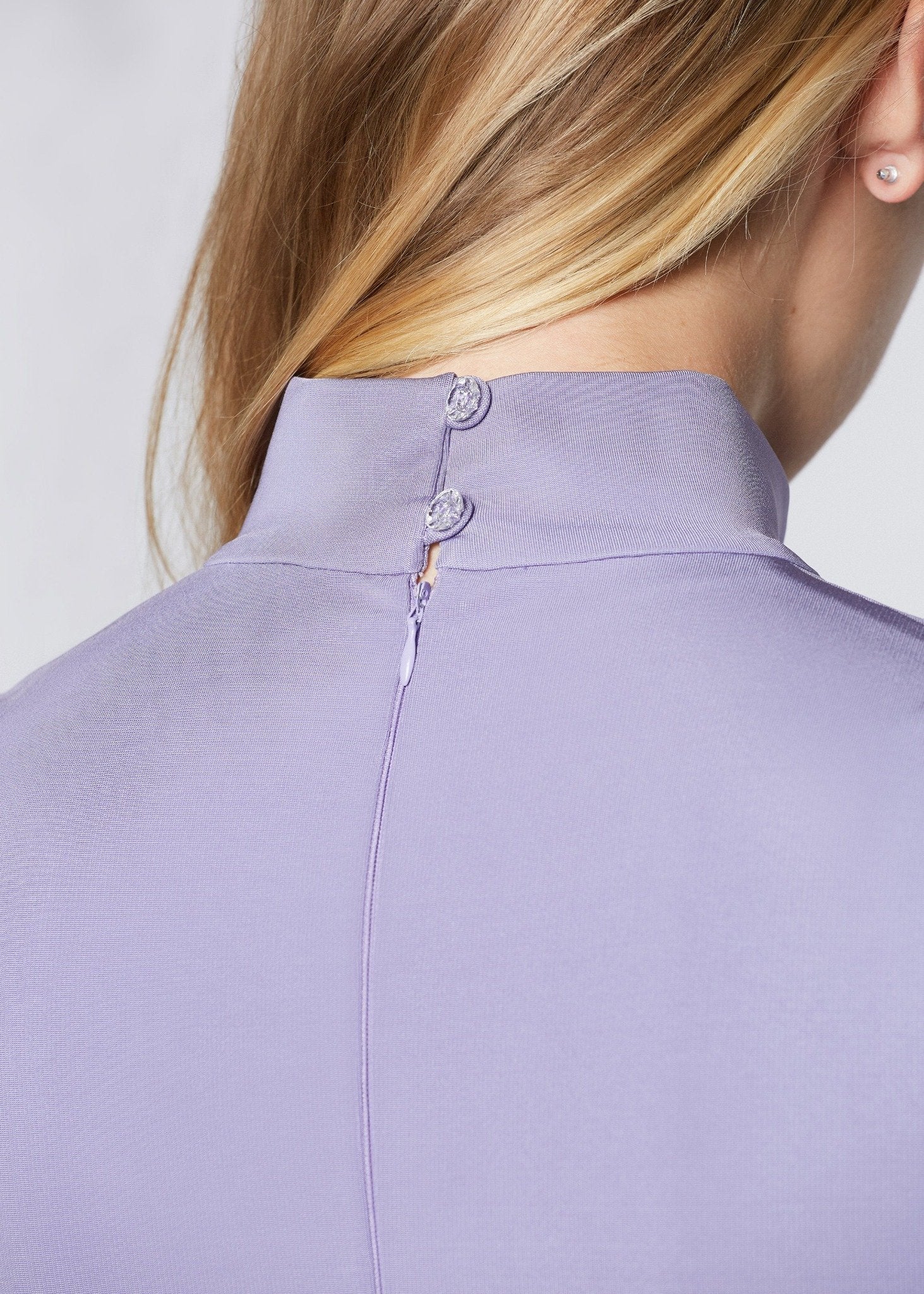 Detailed back view of a woman wearing an asymmetric mock neck fuller bust dress with 3/4 length sleeves and side seam pockets in lilac stretch viscose fabric by Miriam Baker.