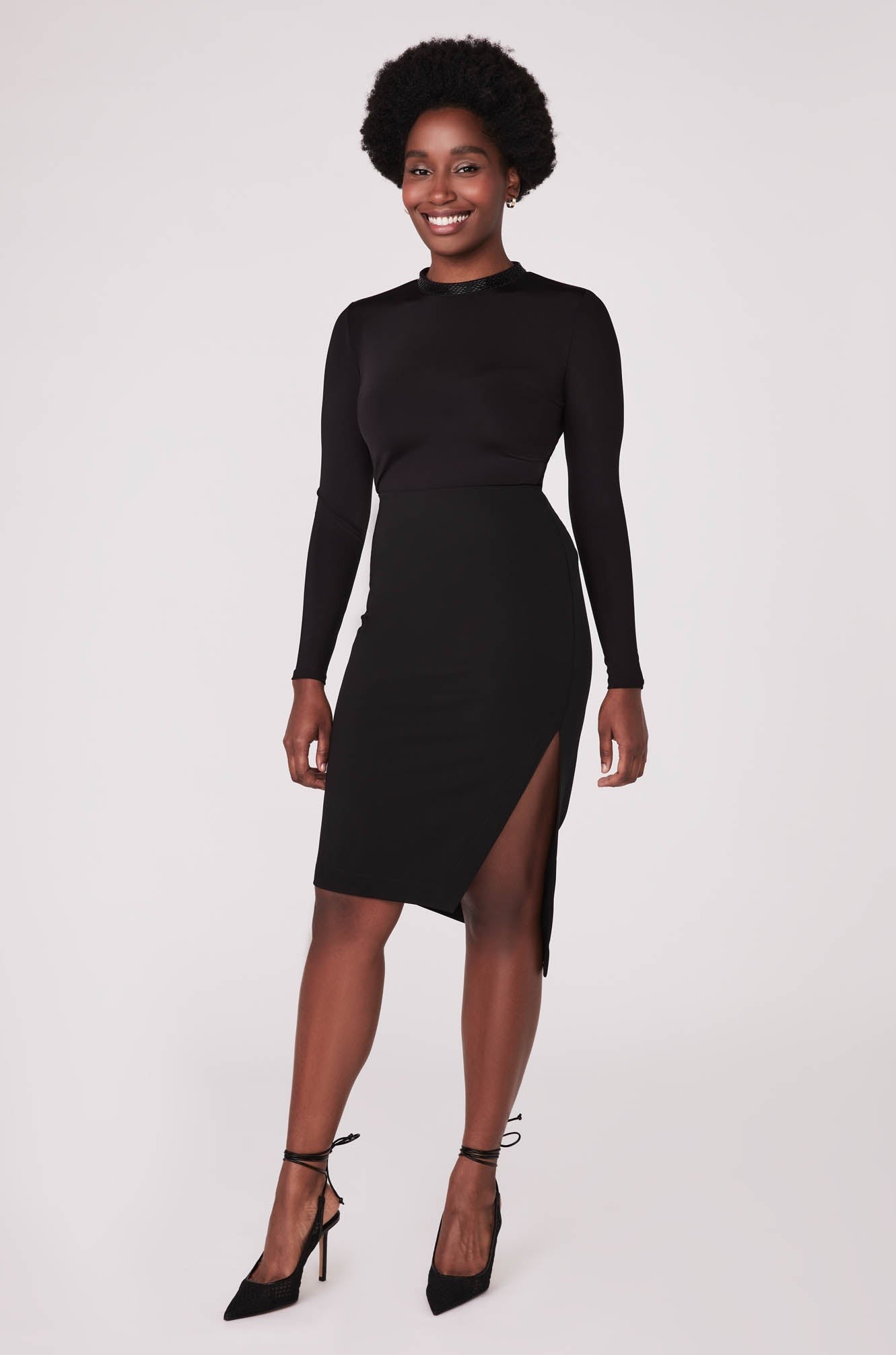 Front view of a woman wearing a high waisted black asymmetrical pencil skirt with cut out by Miriam Baker.