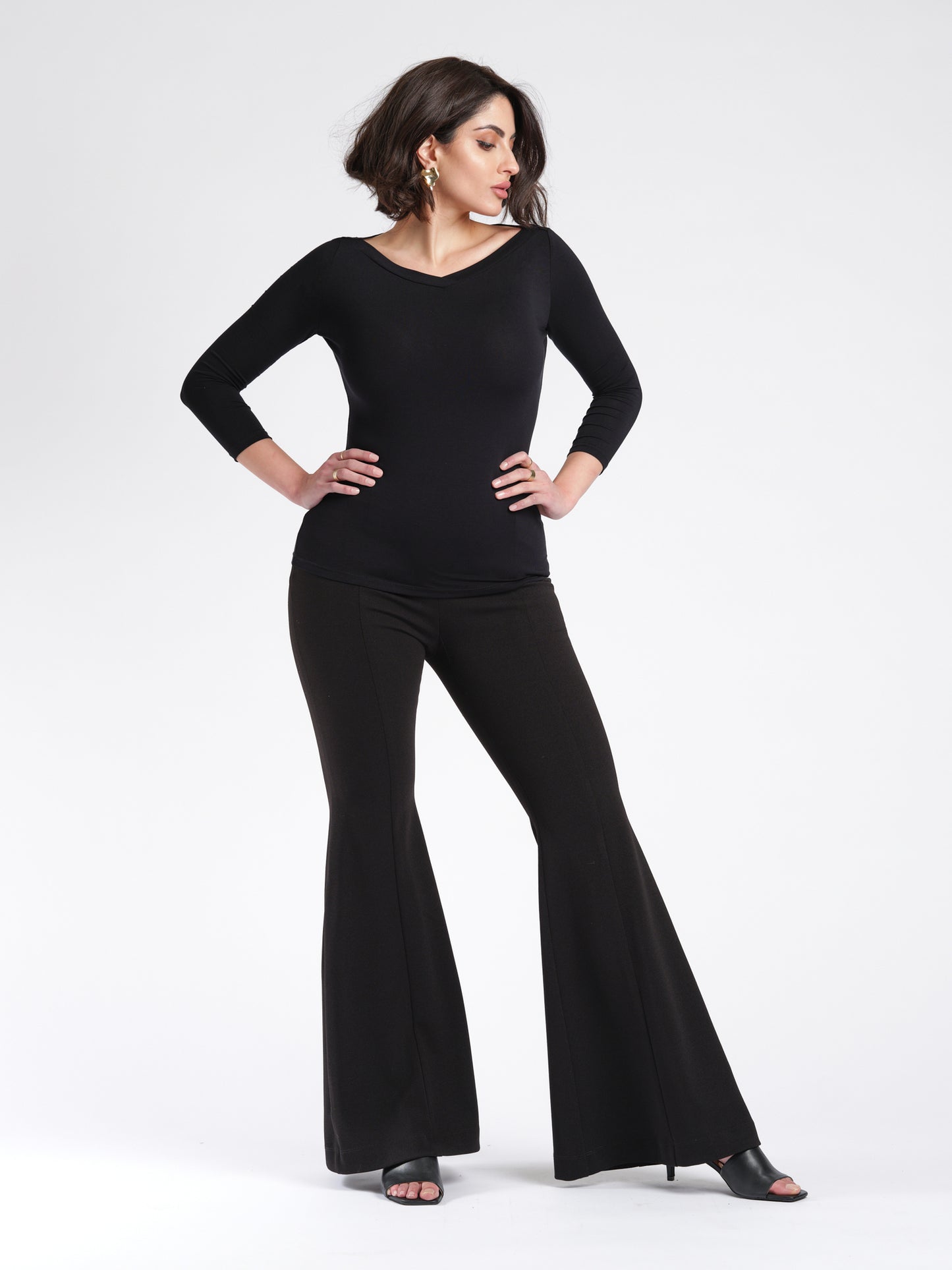 Woman wearing a black 3/4 length sleeve fuller bust bamboo pullover with stylized boatneck paired with bell bottom pants by Miriam Baker.