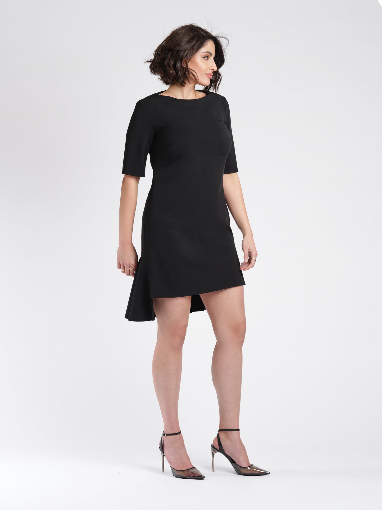 Side view of a woman wearing a black stretch viscose half sleeve crew neck fuller bust t-shirt dress with high low ruffle hem designed by Miriam Baker.
